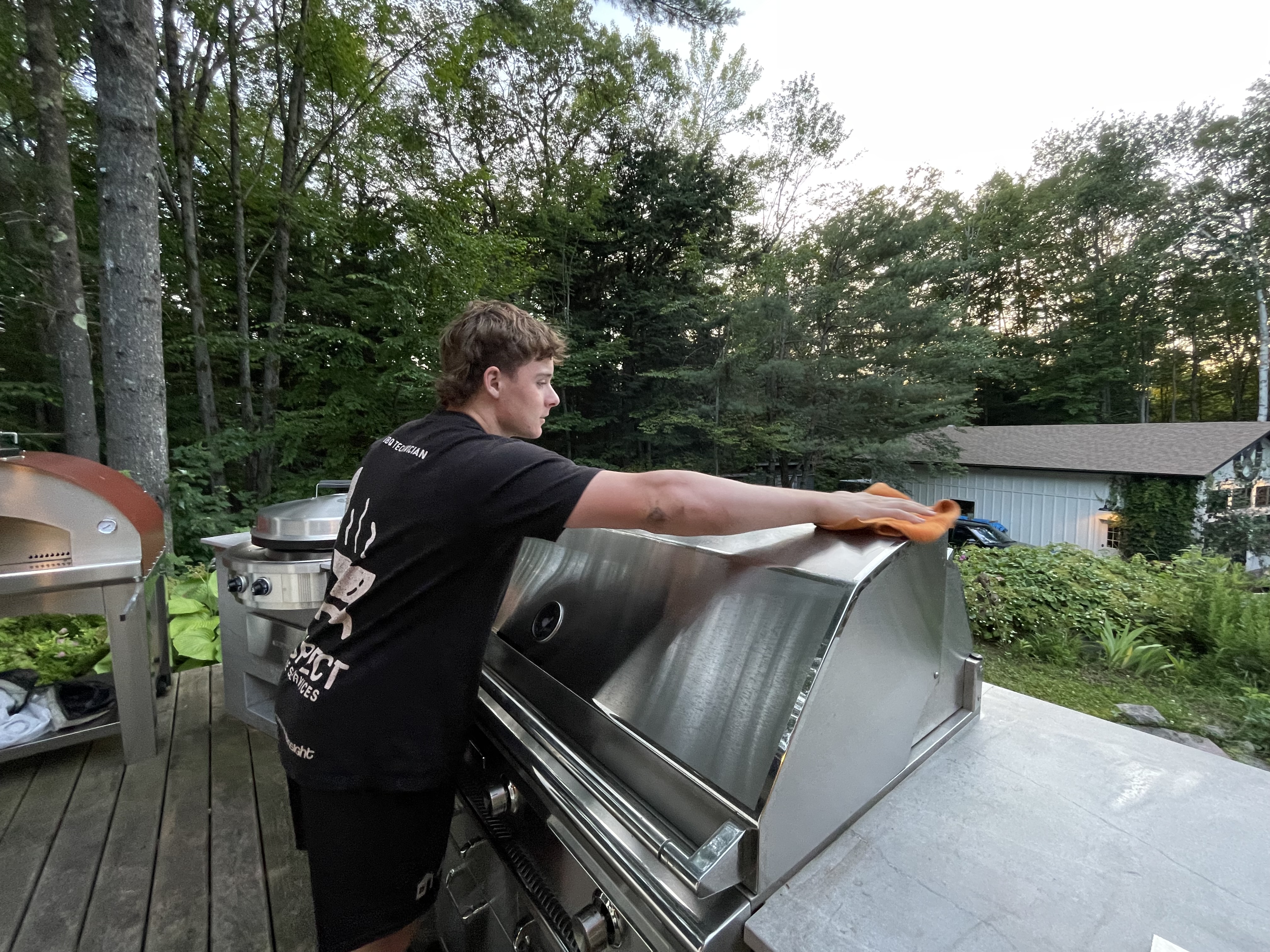 Cleaning a stainless BBQ on a cottage deck at golden hour