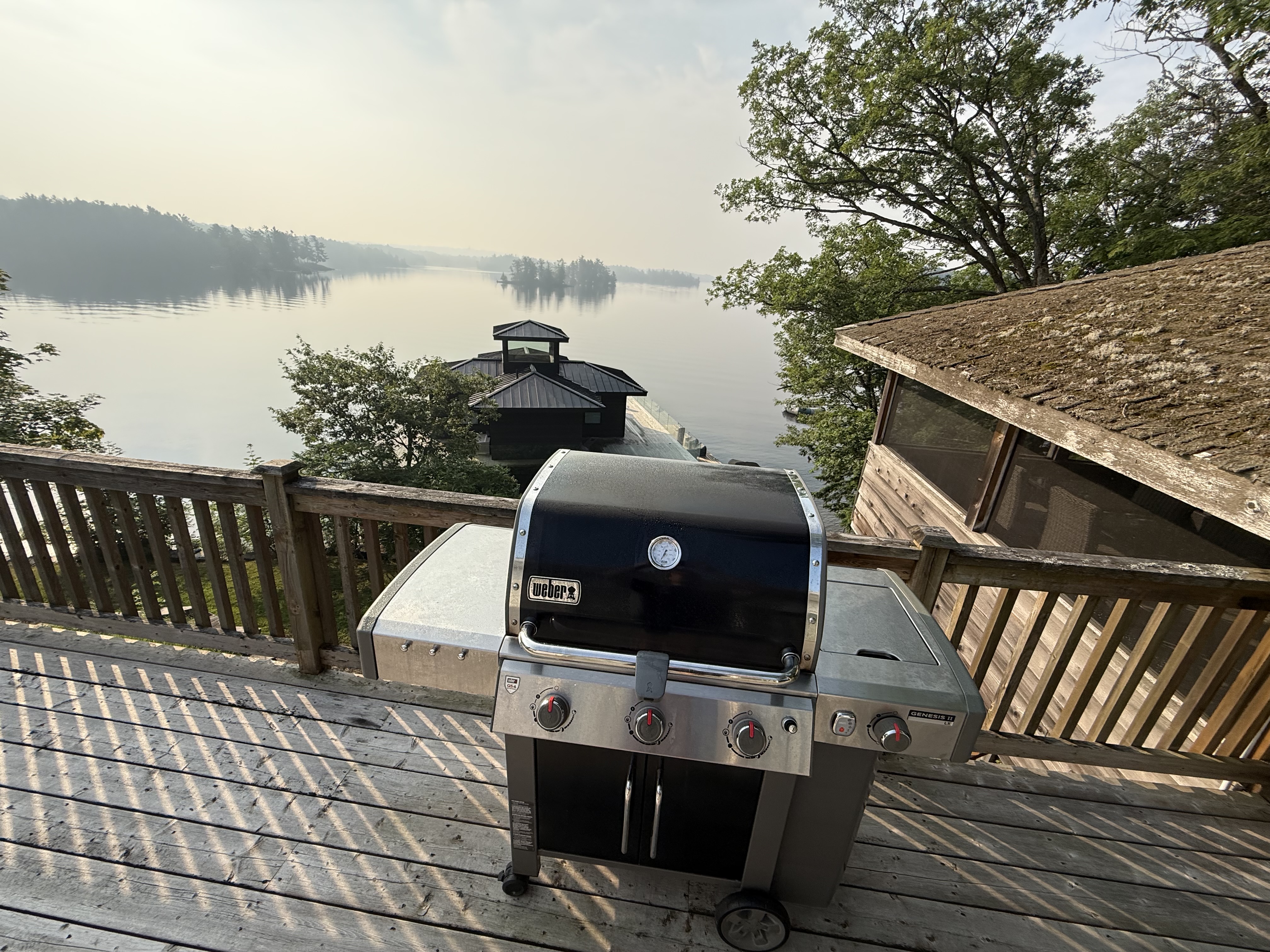 Weber gas grill on a cottage deck with misty lake